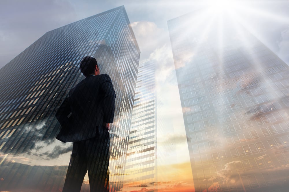 Businessman standing with hands on hips against low angle view of skyscrapers at sunset