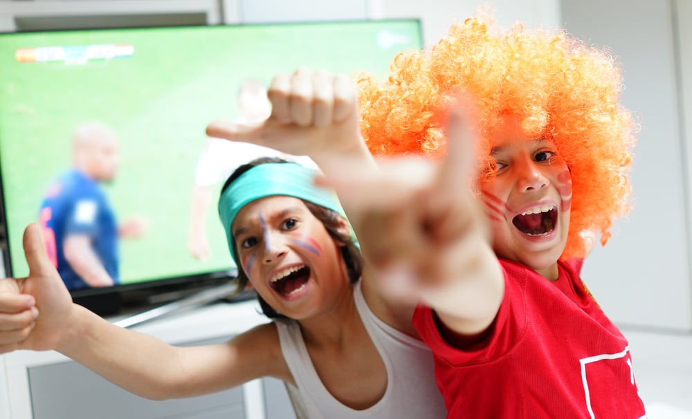 Family with football watching soccer world cup game on tv in living room