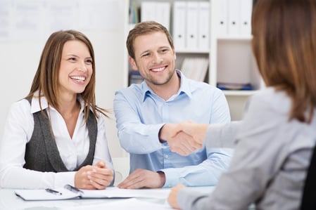 Smiling young man shaking hands with an insurance agent or investment adviser as he sits in a meeting with his wife in her office-1