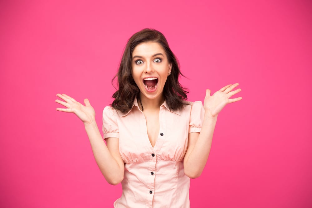 Surprised young woman shouting over pink background. Looking at camera