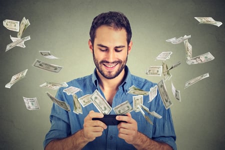 Technology online banking money transfer, e-commerce concept. Happy young man using smartphone with dollar bills flying away from screen isolated on gray wall office background.-2