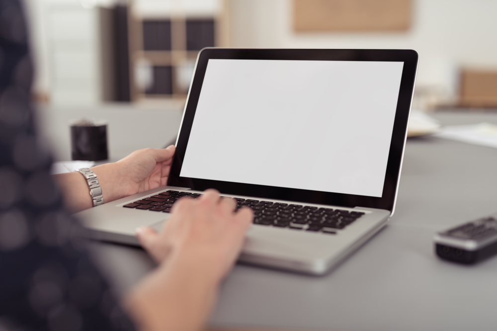 Businesswoman sitting at her desk navigating the internet on a laptop computer using the trackpad, over the shoulder view of the blank screen-2