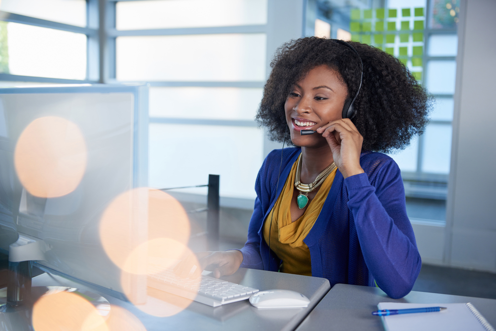 Portrait of a smiling customer service representative with an afro at the computer using headset-1