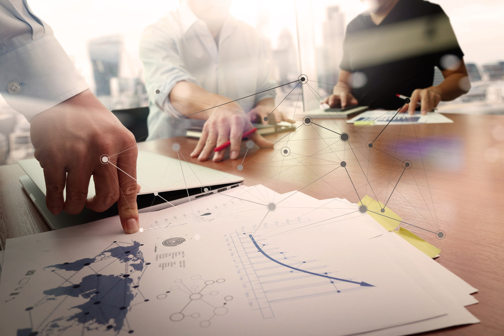 business documents on office table with smart phone and laptop computer and graph financial with social network diagram and two colleagues discussing data in the background-3