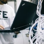 サーバールームでネットワーク機器とノートパソコンを確認するエンジニア